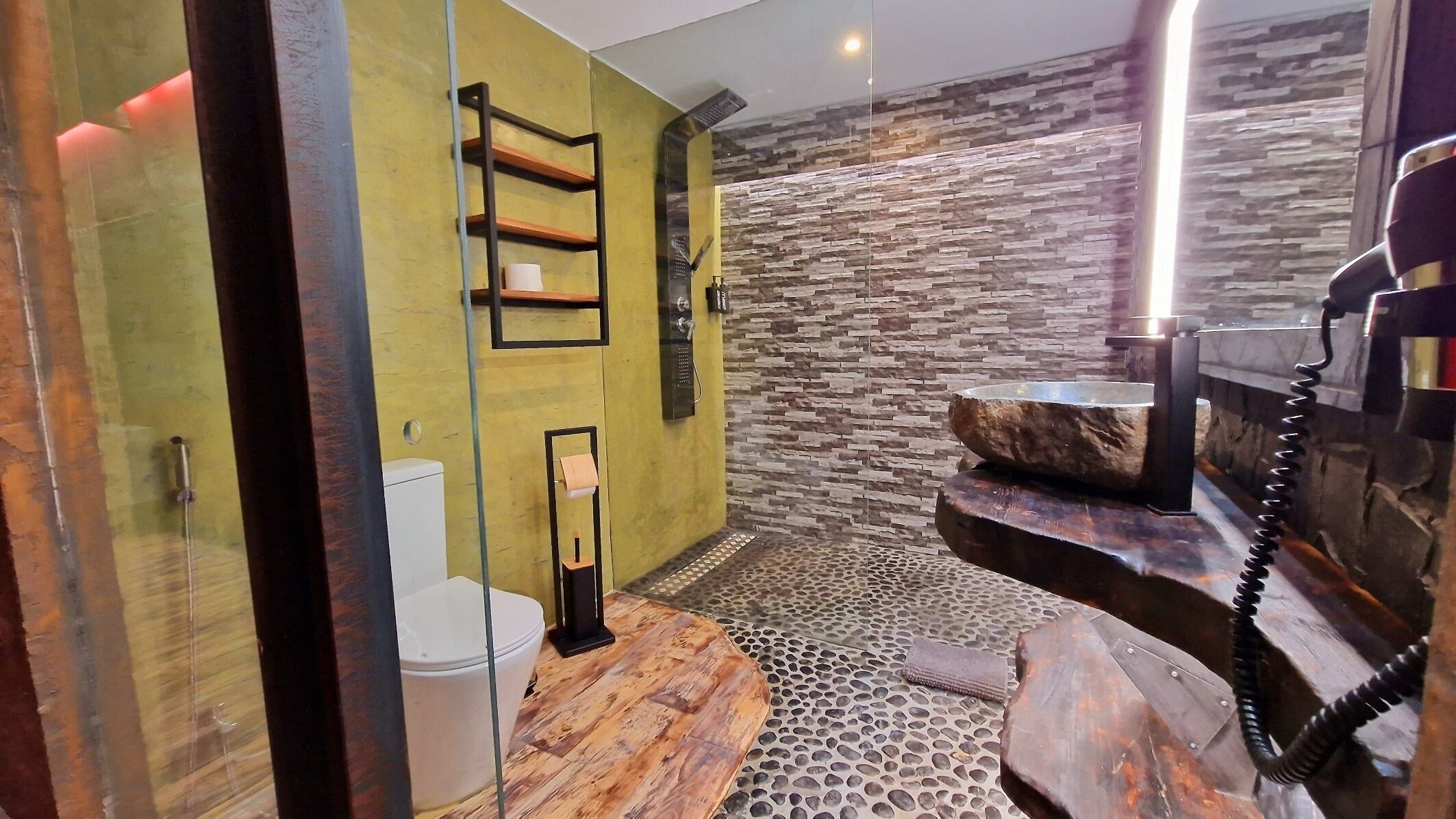 A modern bathroom with a stone wall, a wooden vanity, and a glass shower enclosure.