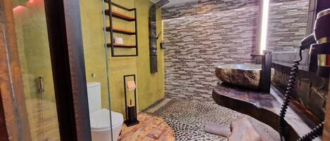A modern bathroom with a stone wall, a wooden vanity, and a glass shower enclosure.