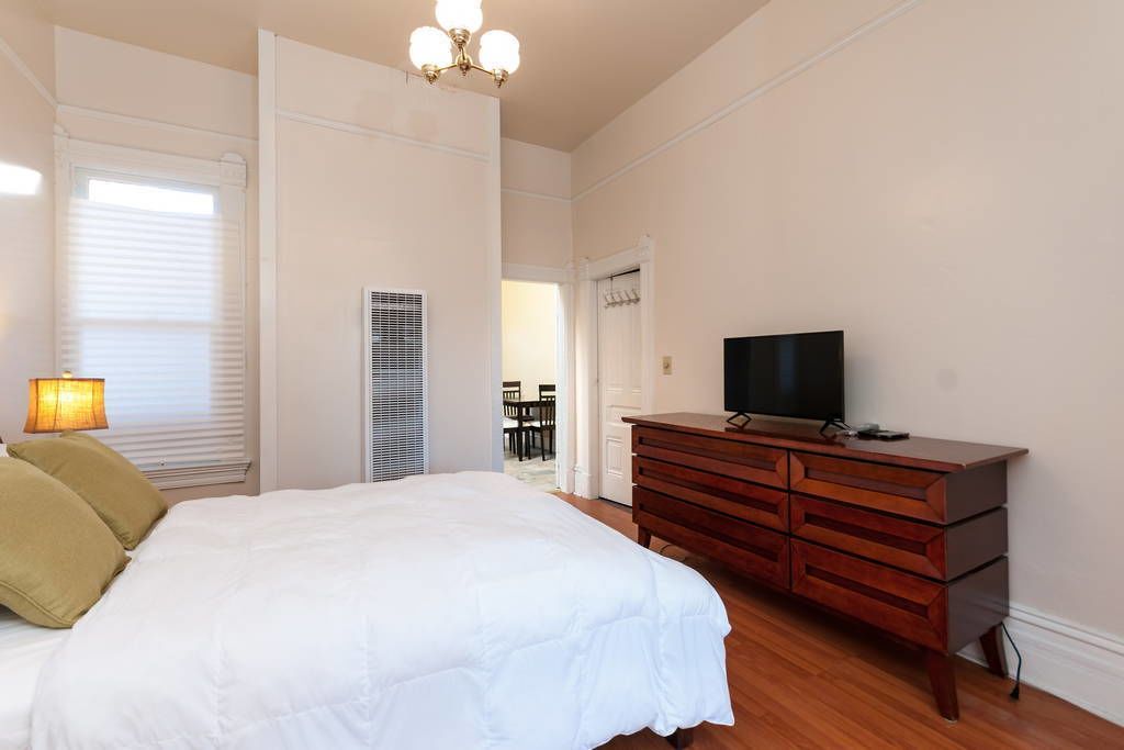A bedroom with a bed, a dresser, a television, and a window with blinds.
