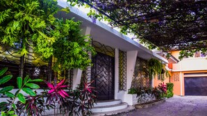 Una casa moderna con fachada blanca, una verja negra y un porche cubierto con plantas.