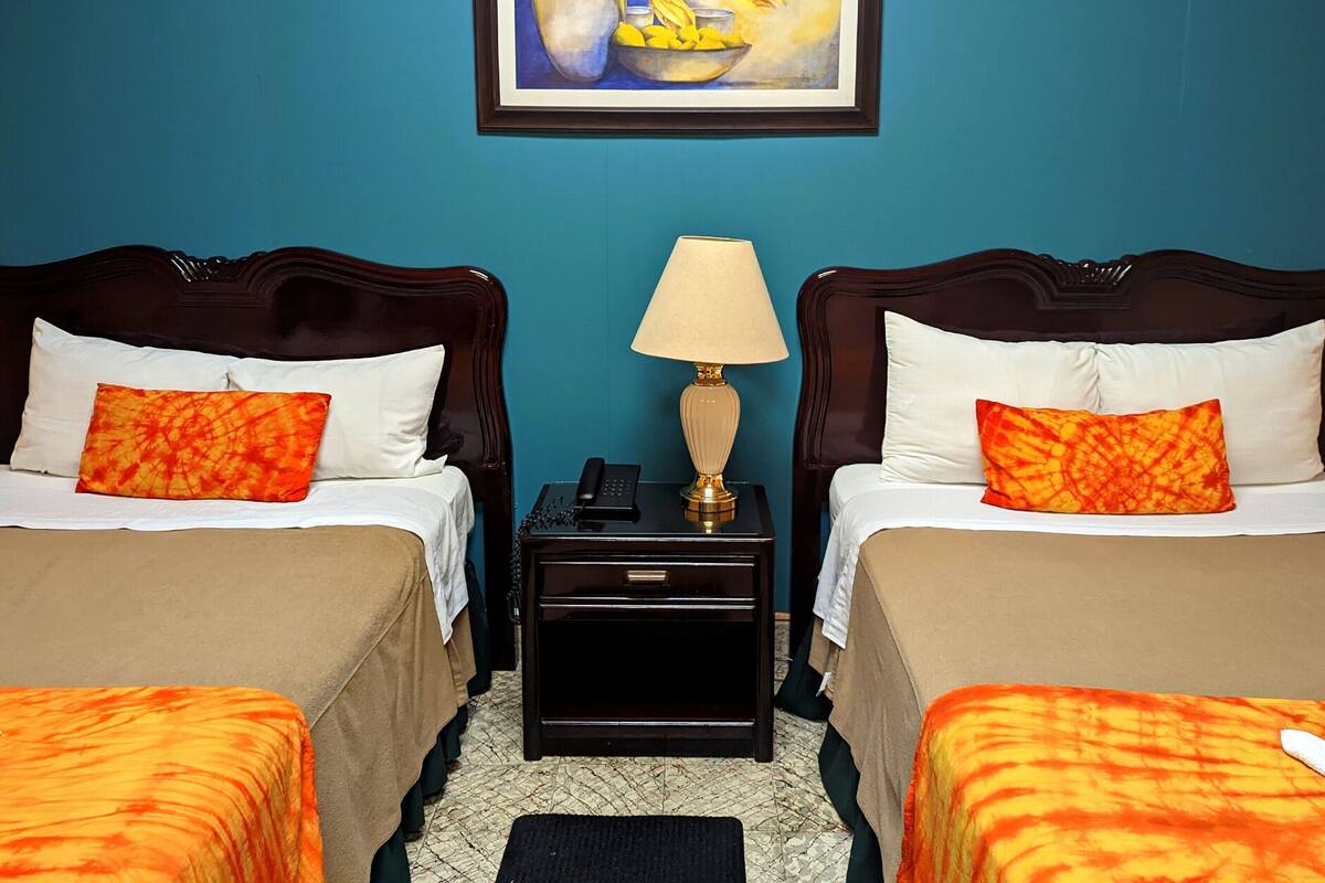 Habitación de hotel con dos camas, una mesita de noche con una lámpara y un cuadro enmarcado en la pared.