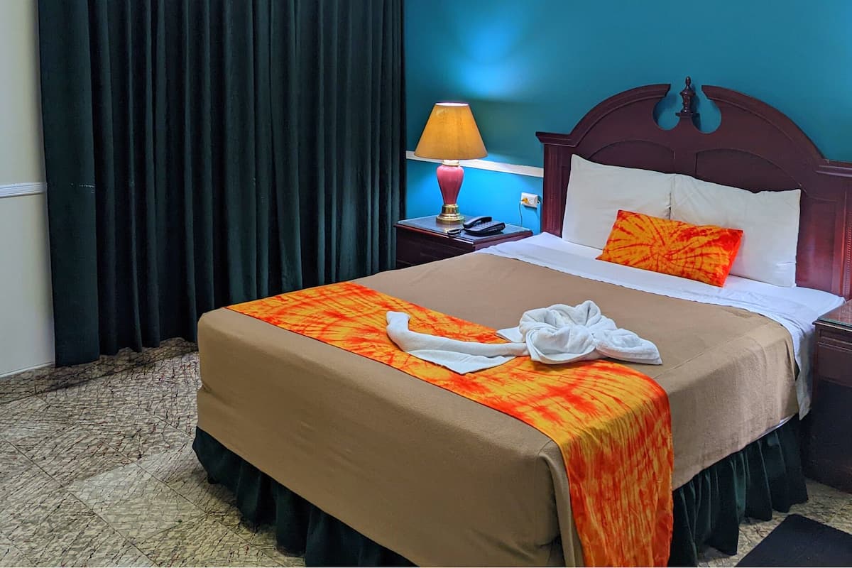 Una habitación de hotel con una cama, una mesita de noche, una lámpara y una cortina.