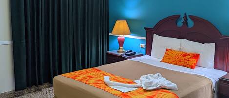 Una habitación de hotel con una cama, una mesita de noche, una lámpara y una cortina.
