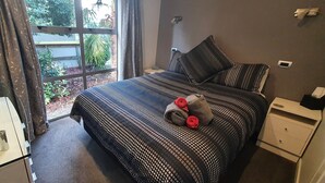 Une chambre à coucher avec un grand lit, une table de chevet, une commode et une fenêtre avec des rideaux.