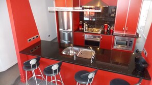 Une cuisine moderne avec des meubles de rangement rouges, des appareils en acier inoxydable et un îlot central doté de tabourets de bar.