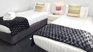 Et hotelværelse med to senge, et sengebord med lampe, et vindue med udsigt over byen og et stabel håndklæder på den venstre seng.