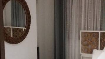 A hotel room with a single bed, a wooden chair, a round mirror, and a window with curtains.