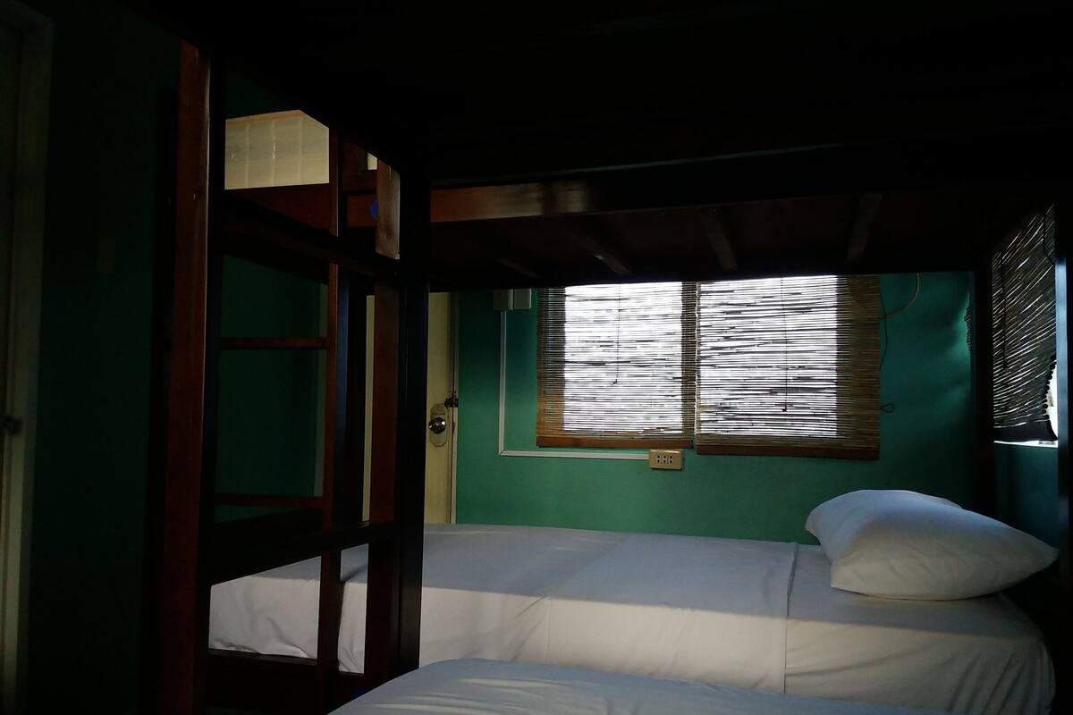 Una habitación con dos camas, un ventanal con persianas y una puerta con lámpara.