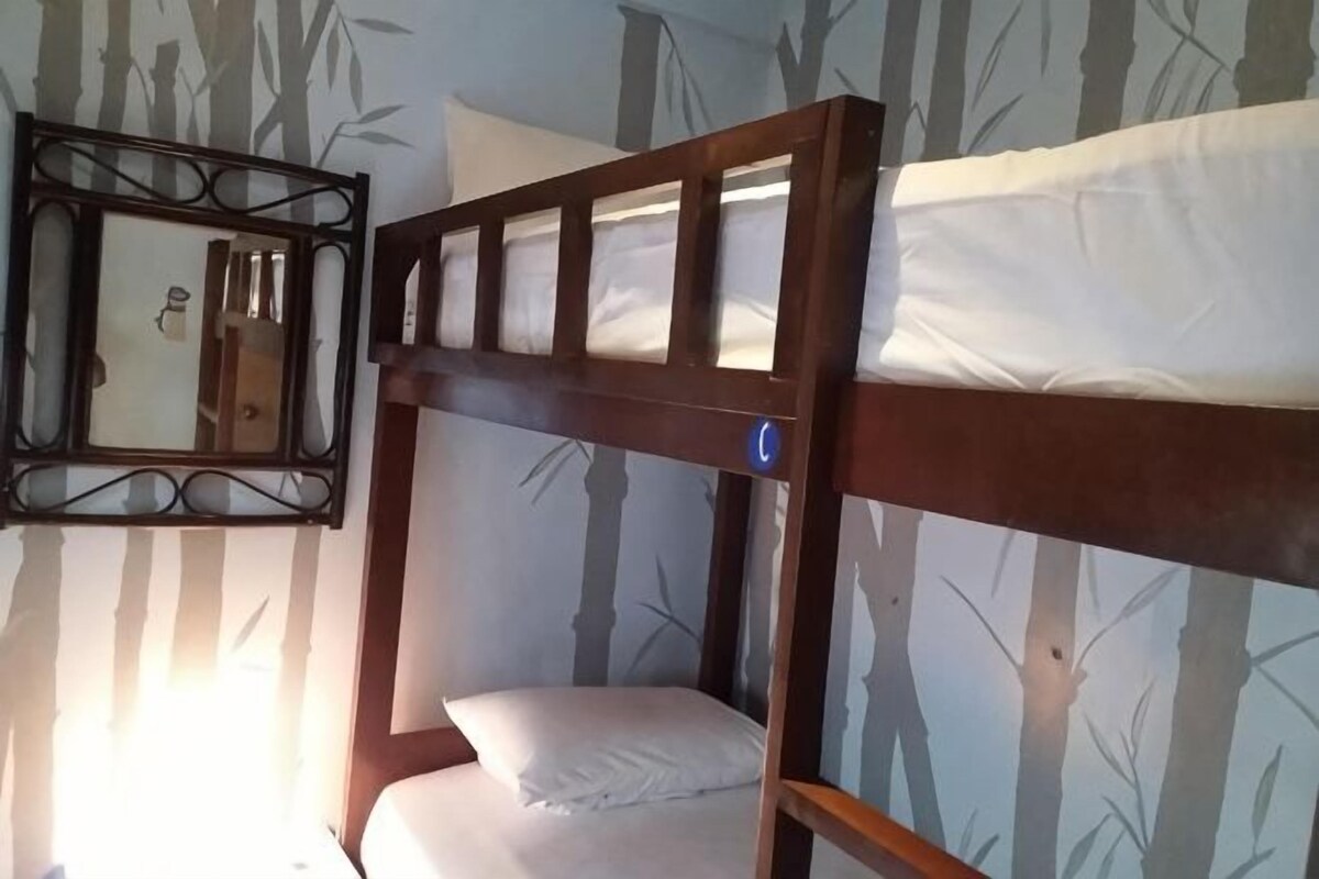 A bunk bed with a wooden frame and white bedding, a mirror with a decorative frame, and a wall with a bamboo pattern.