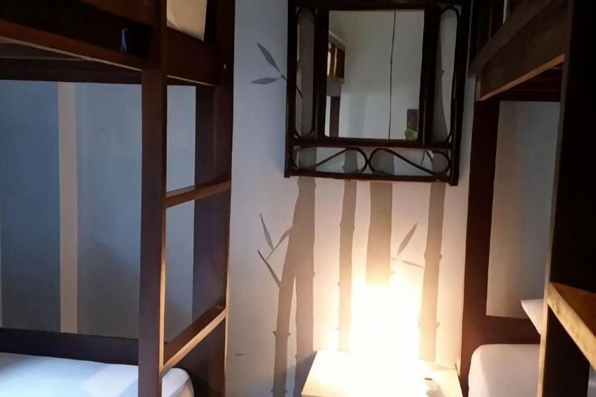 Una habitación con literas, un espejo y una ventana con persianas verticales.
