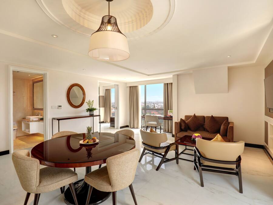A spacious living area with a round dining table, comfortable seating, a large window with a city view, and a modern ceiling design.