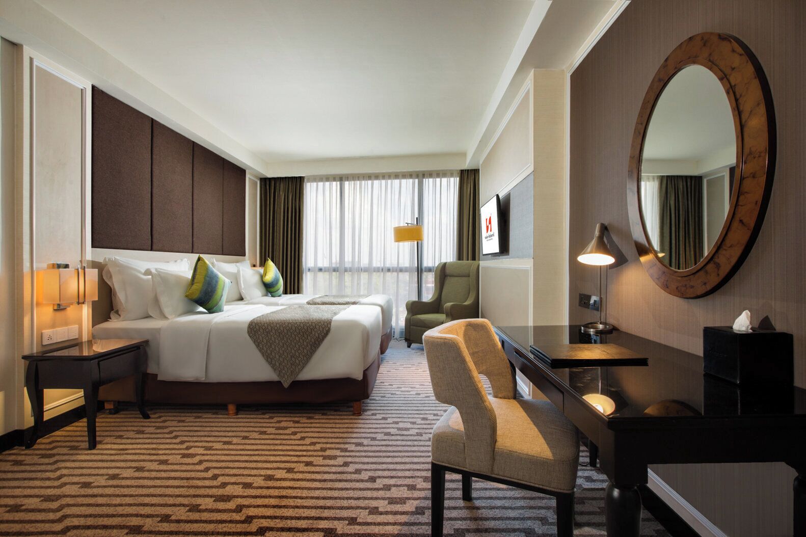 Une chambre d’hôtel avec un grand lit, un bureau, une chaise, un miroir et un sol recouvert de moquette.