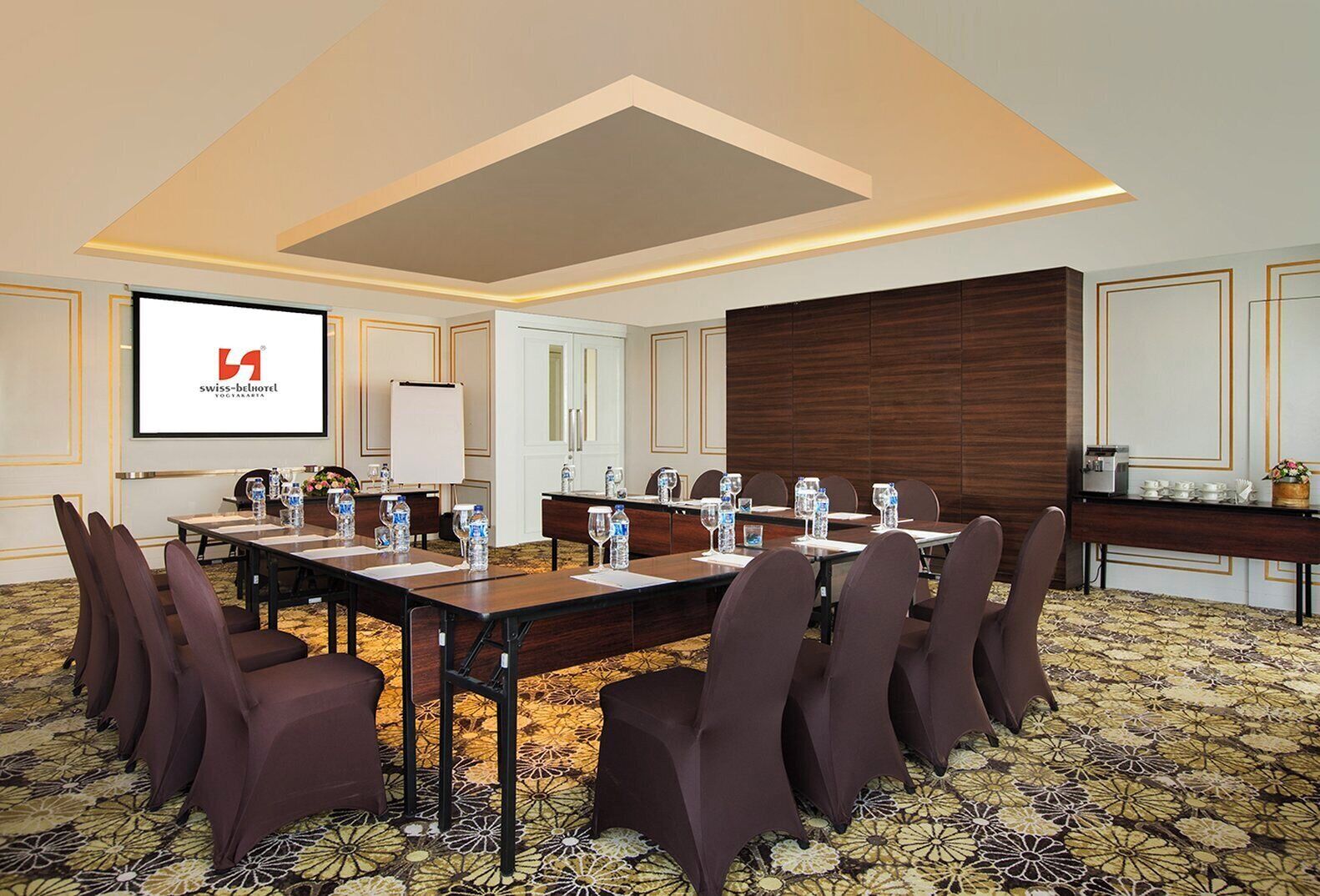 A conference room with a long table, chairs, and a projector screen displaying the Swiss-Belhotel logo.