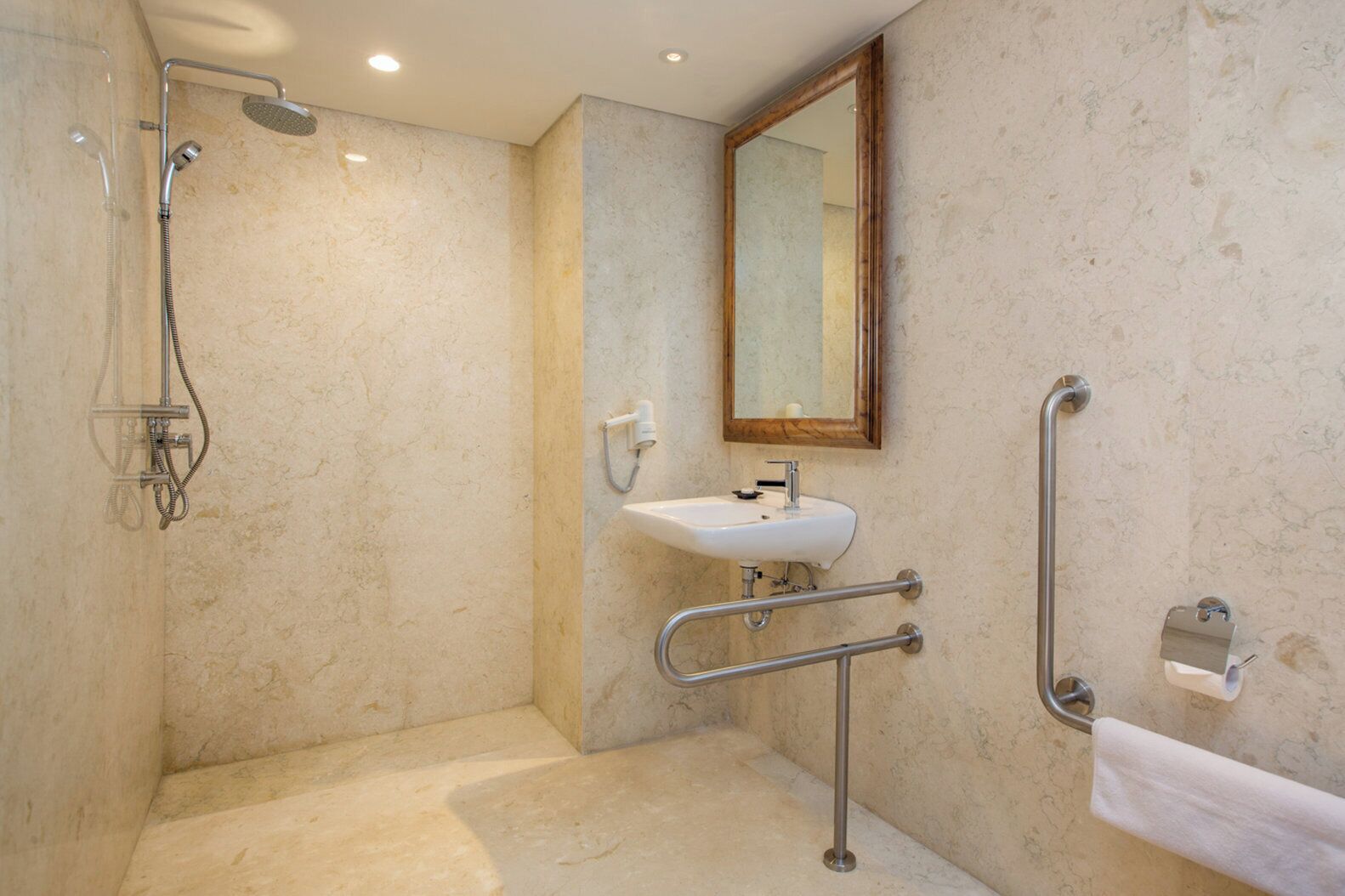 Ein Badezimmer mit Dusche, Waschbecken, Spiegel und Haltegriff.