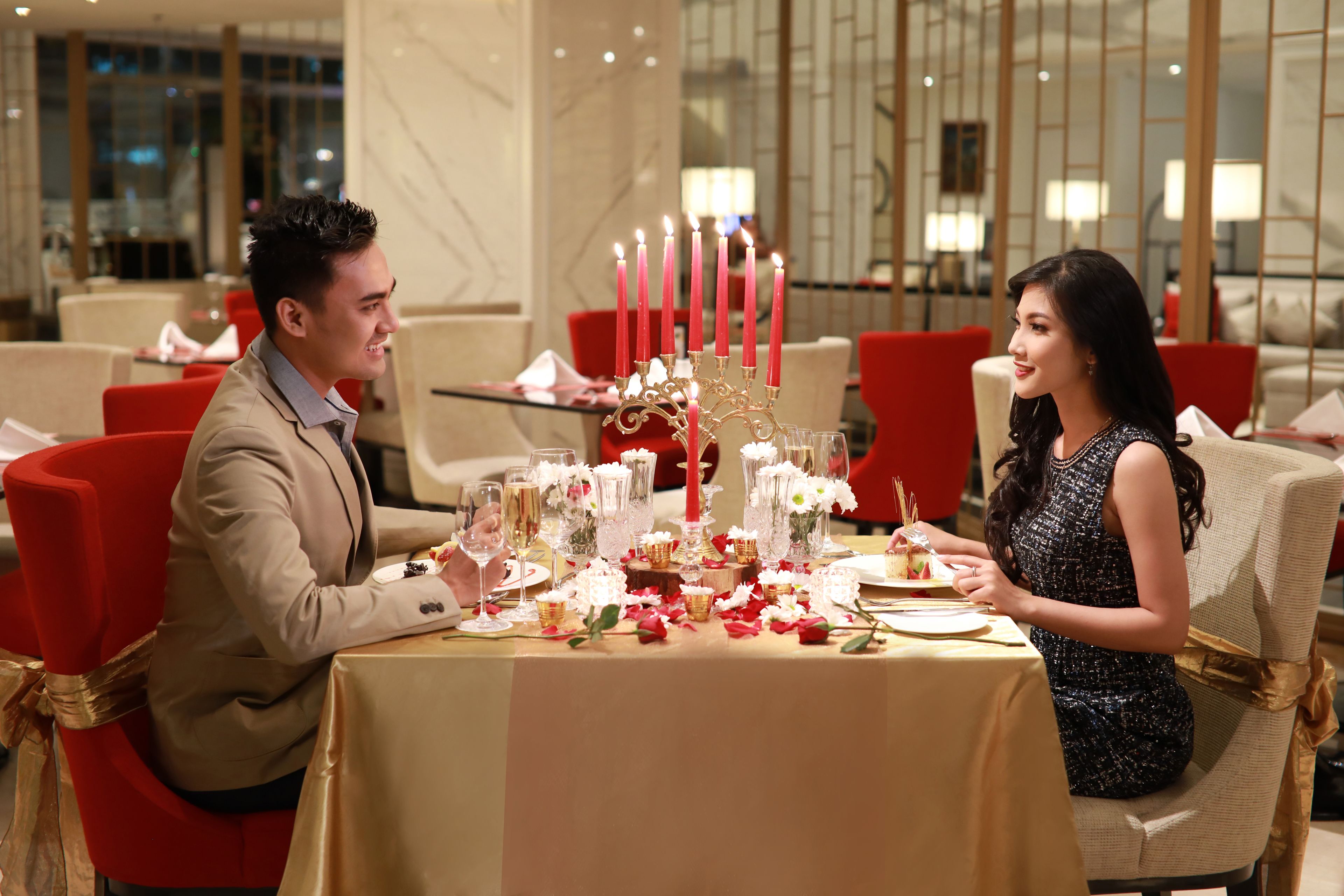 Mesa de comedor dispuesta con velas, vasos y adornos florales en un interior moderno con sillas rojas y una silla dorada.