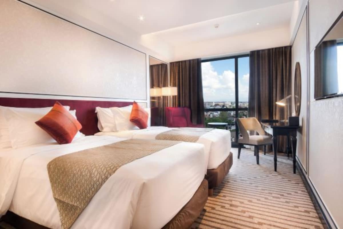 Una habitación de hotel con dos camas, un escritorio, una silla y un ventanal con vistas a la ciudad.