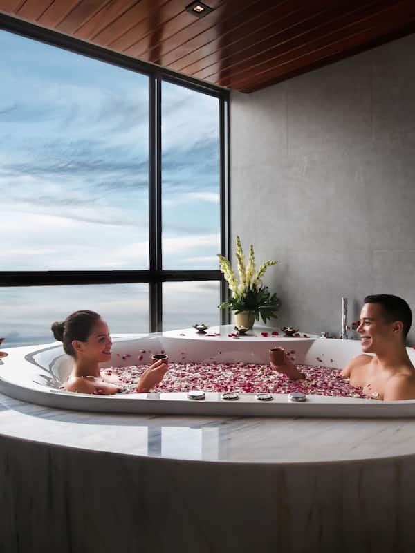 Relax in a serene bathroom with a large bathtub, a view of the sky, and a charming table setting.