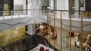 Un vestíbulo amplio con techo alto, un área de estar central con un sofá y sillones, y un comedor con mesas y sillas.