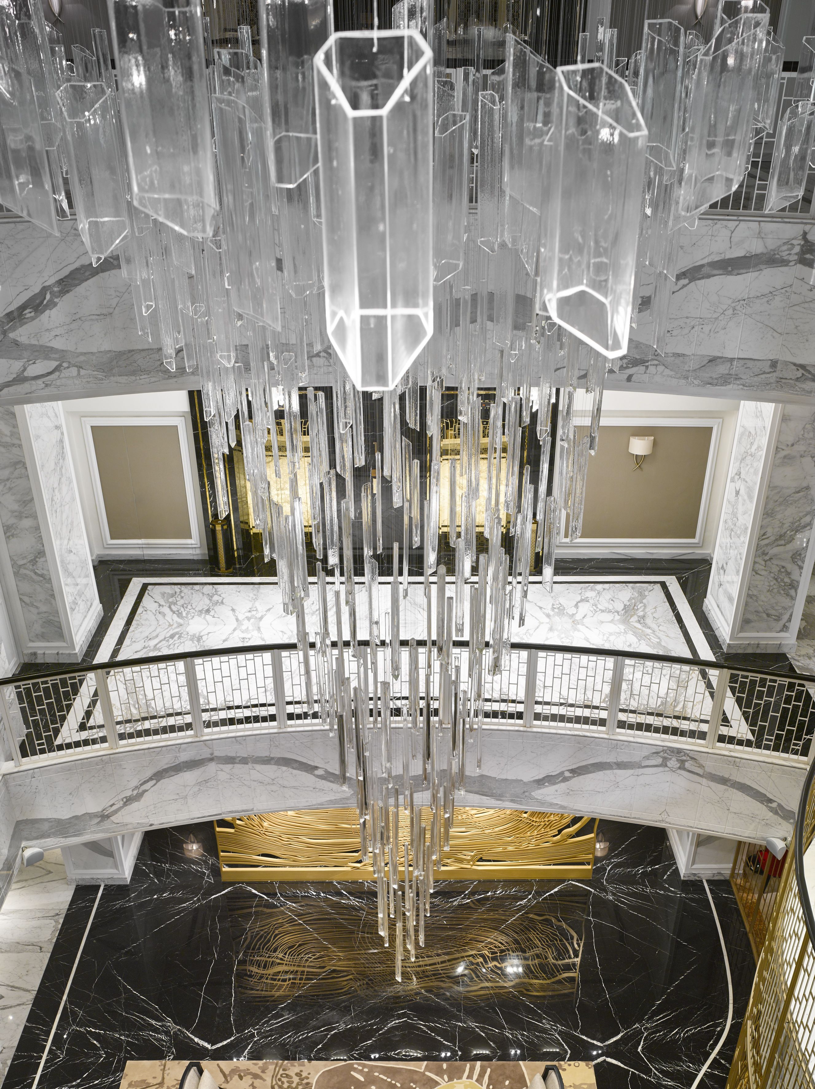 Un hall imponente con piso de mármol, una lámpara central y una escalera con barandilla.