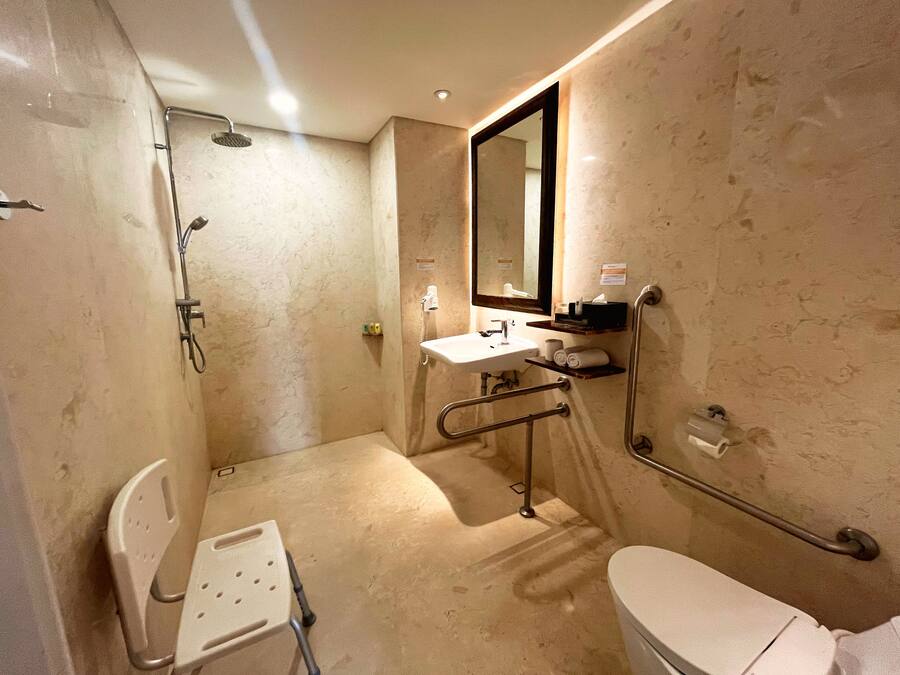 A bathroom with a shower, toilet, sink, and a wheelchair-accessible chair.