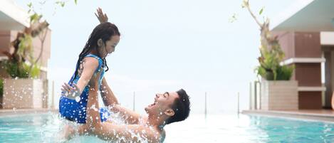 A man and a woman in a swimming pool with clear water, surrounded by buildings.