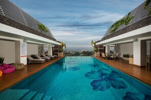 Uma piscina interior moderna com água azul cristalina, espreguiçadeiras e vista para a cidade ao fundo.