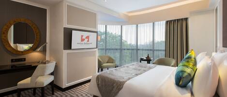 Habitación de hotel con una cama grande, un escritorio con silla, un espejo redondo y vistas al exterior a través de amplios ventanales.
