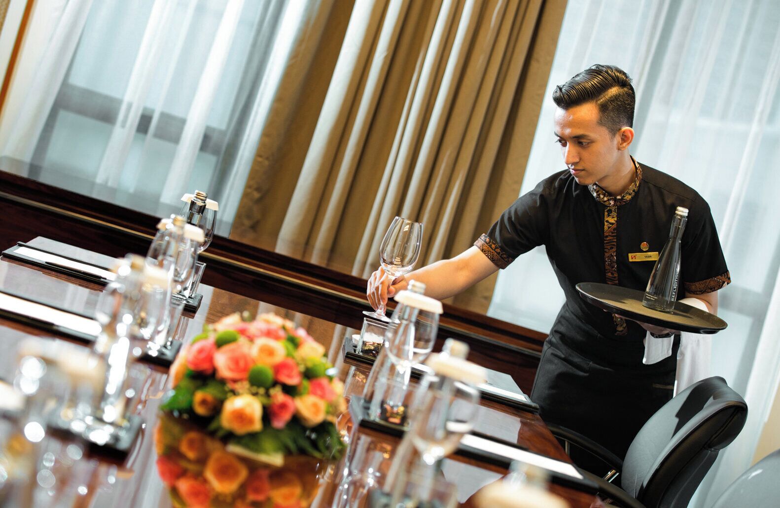 A hotel staff member setting a table with wine glasses and a floral centerpiece.