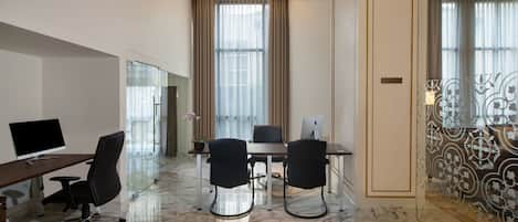 Une chambre d’hôtel moderne avec un sol en marbre, un bureau avec un ordinateur, deux chaises, une grande fenêtre avec des rideaux et un panneau décoratif mural.