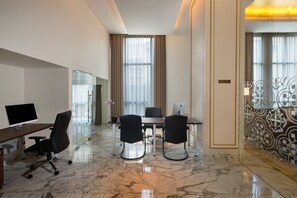 A modern hotel room with a marble floor, a desk with a computer, two chairs, a large window with curtains, and a decorative wall panel.