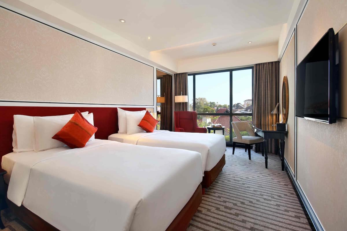 Ein Hotelzimmer mit zwei Betten, einem Fernseher, einem Schreibtisch und Blick auf die Stadt.