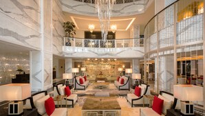 Un vestíbulo espacioso con techos altos, paredes de mármol y una zona de estar central con sofás y sillones.