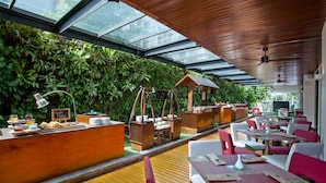 Un restaurante con mostrador de madera, sillas rojas y blancas, y una pared verde con plantas.