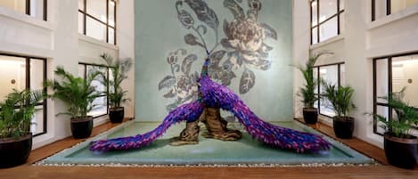 Un vestíbulo espacioso con un gran mural de un pavo real, plantas en macetas y piso de madera.
