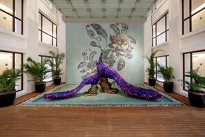 A spacious lobby with a large mural of a peacock, potted plants, and a wooden floor.
