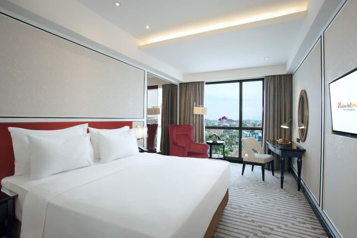 Ein Hotelzimmer mit einem großen Bett, einem Schreibtisch, einem Sessel und Blick auf die Stadt.