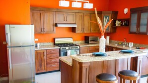 A kitchen with wooden cabinets, a stainless steel refrigerator, a gas stove, and a central island with stools. - Skyview Manor Guest Apartments (Kingston)