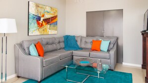 A modern living room with a grey sectional sofa, a glass coffee table, and a teal rug. - Skyview Manor Guest Apartments (Kingston)