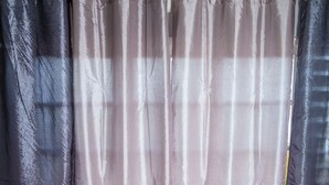 A room with two wooden chairs, a small table with a vase of flowers, and a curtain with a subtle pattern. - Skyview Manor Guest Apartments (Kingston)