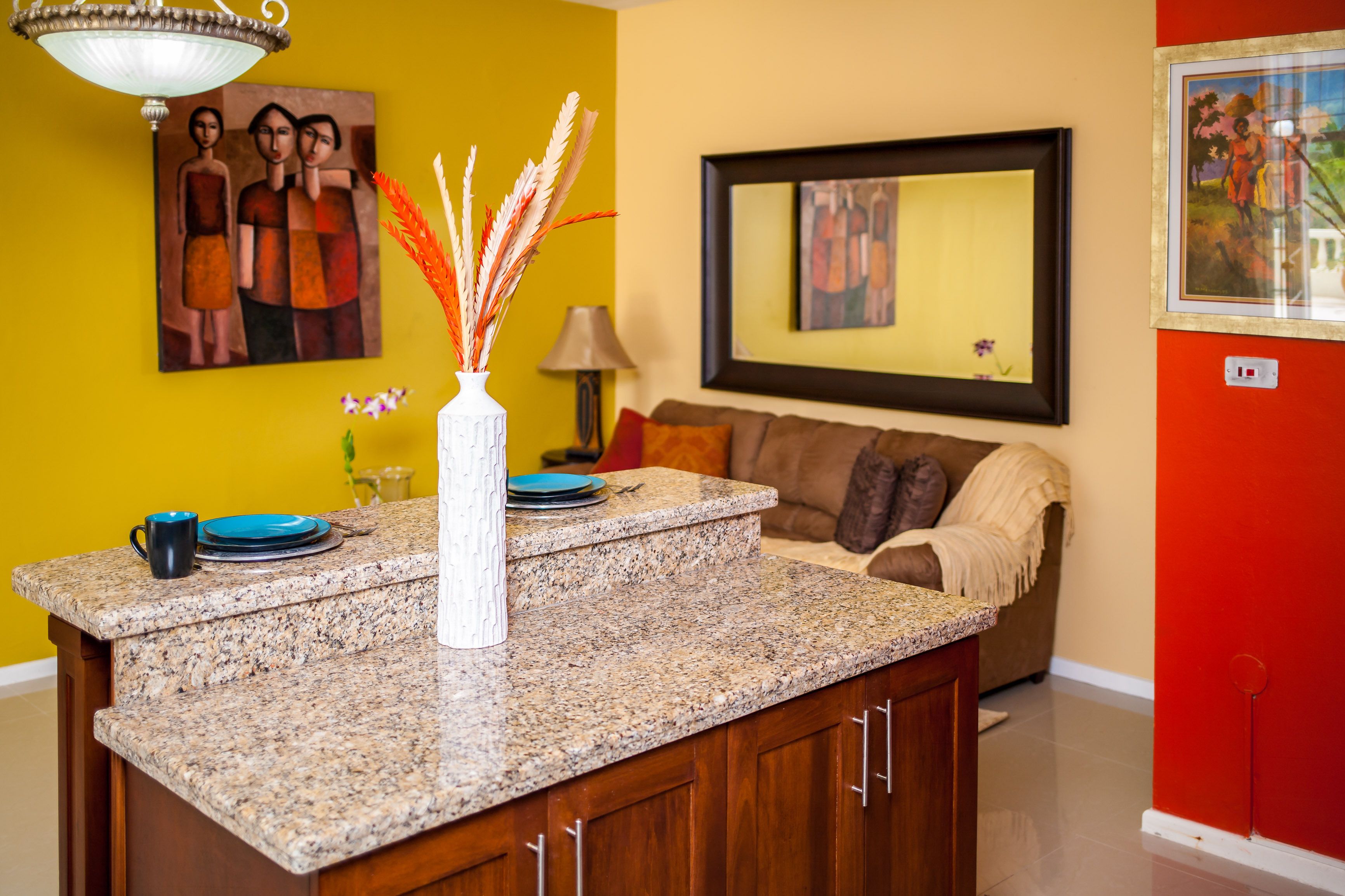 A kitchen with granite countertops, a white vase with dried plants, and a brown sofa in the background.