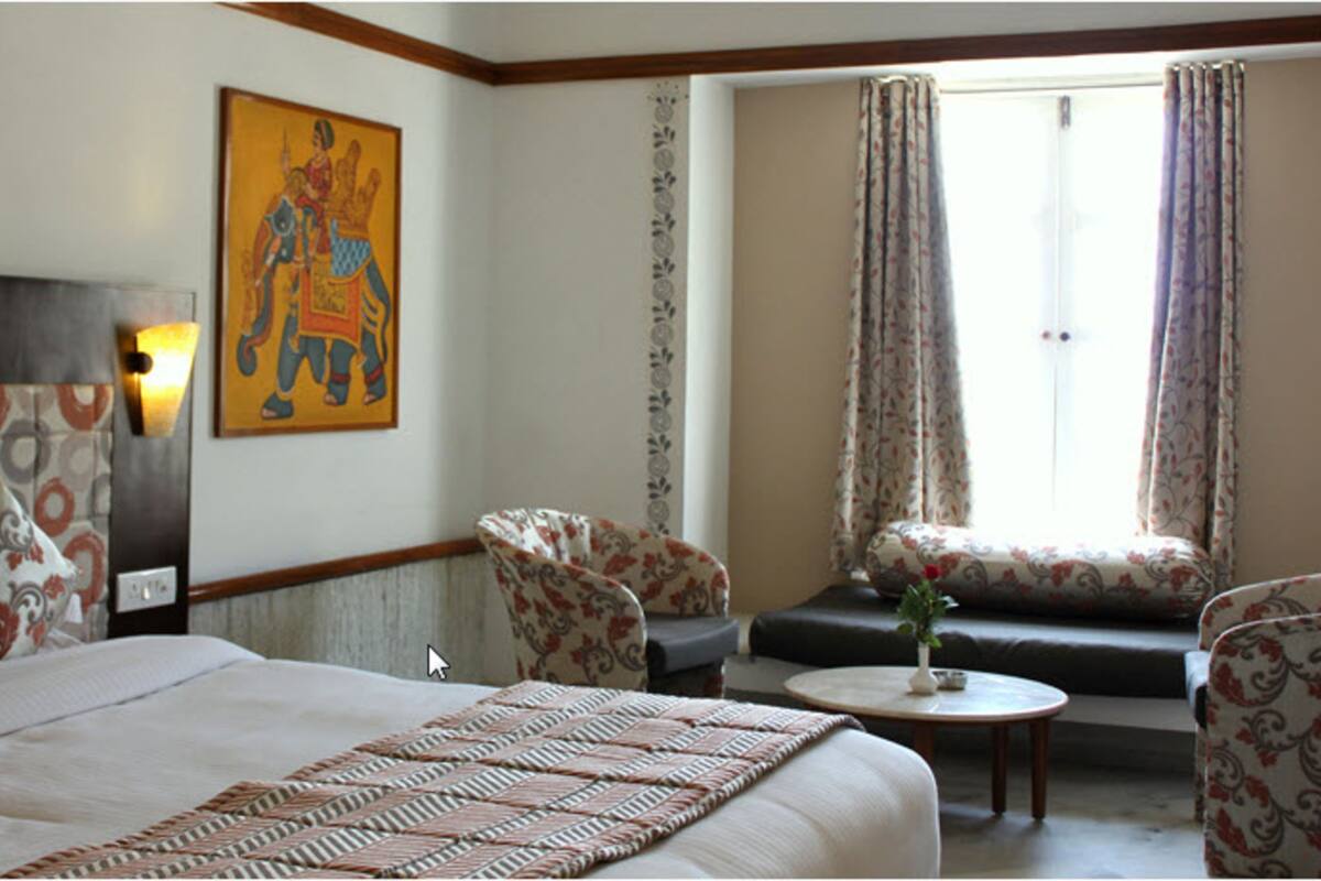 A hotel room with a bed, two armchairs, a sofa, a small table with a vase, and a window with curtains.