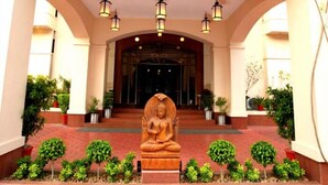 Entrada de um edifício com estátua de Buda, plantas em vasos e lanternas penduradas.