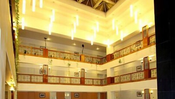 Um hall de hotel com vários níveis, uma escadaria central e um design de lustre moderno.