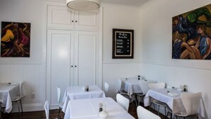 Een eetgedeelte met witte tafels en stoelen, een menubord en twee schilderijen aan de muur.