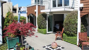 Een modern gebouw met een balkon, een patio met stoelen en een tuin met een boom met rode bladeren.
