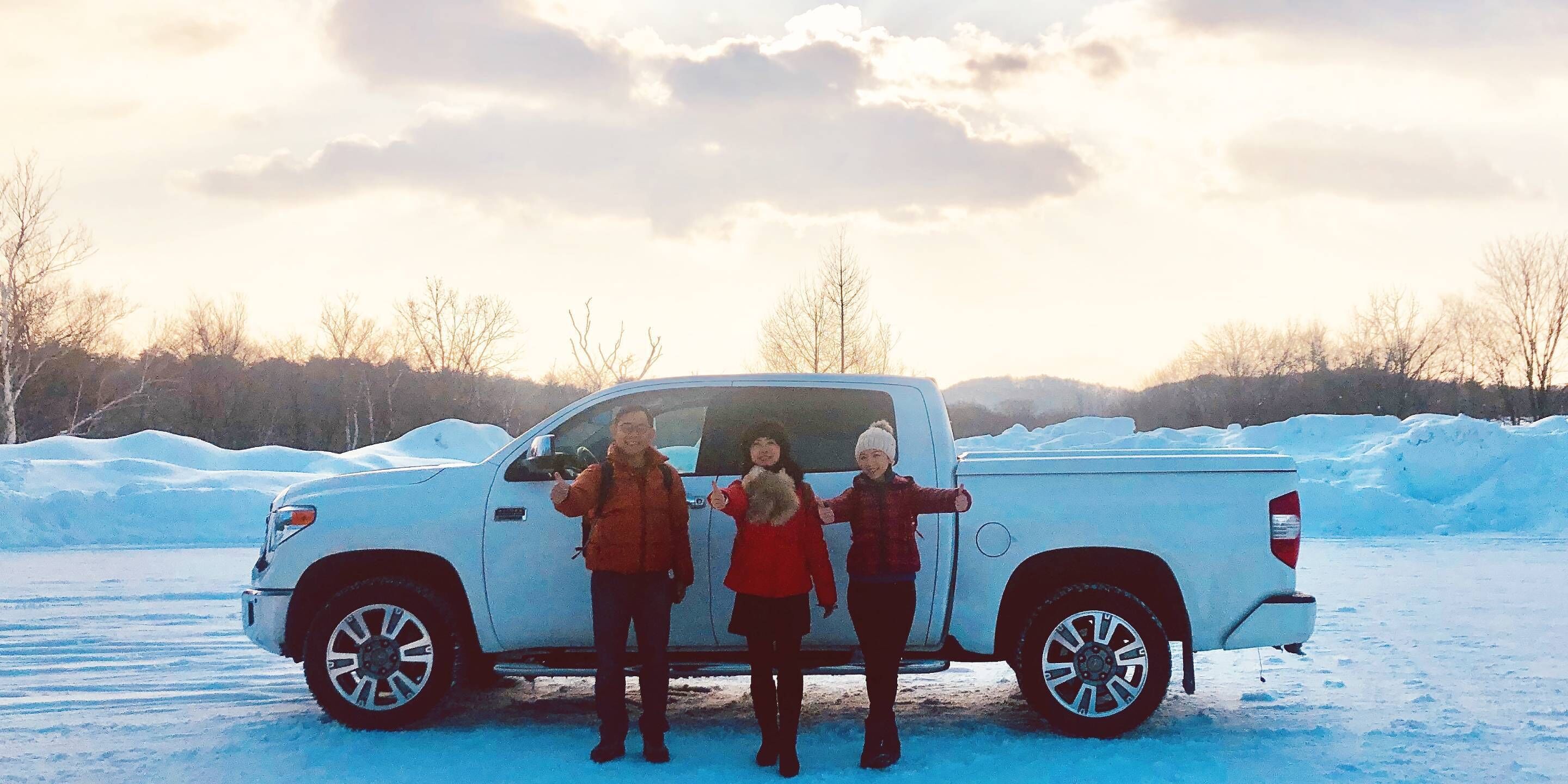 A white pickup truck parked on a snowy surface with three people standing beside it.
