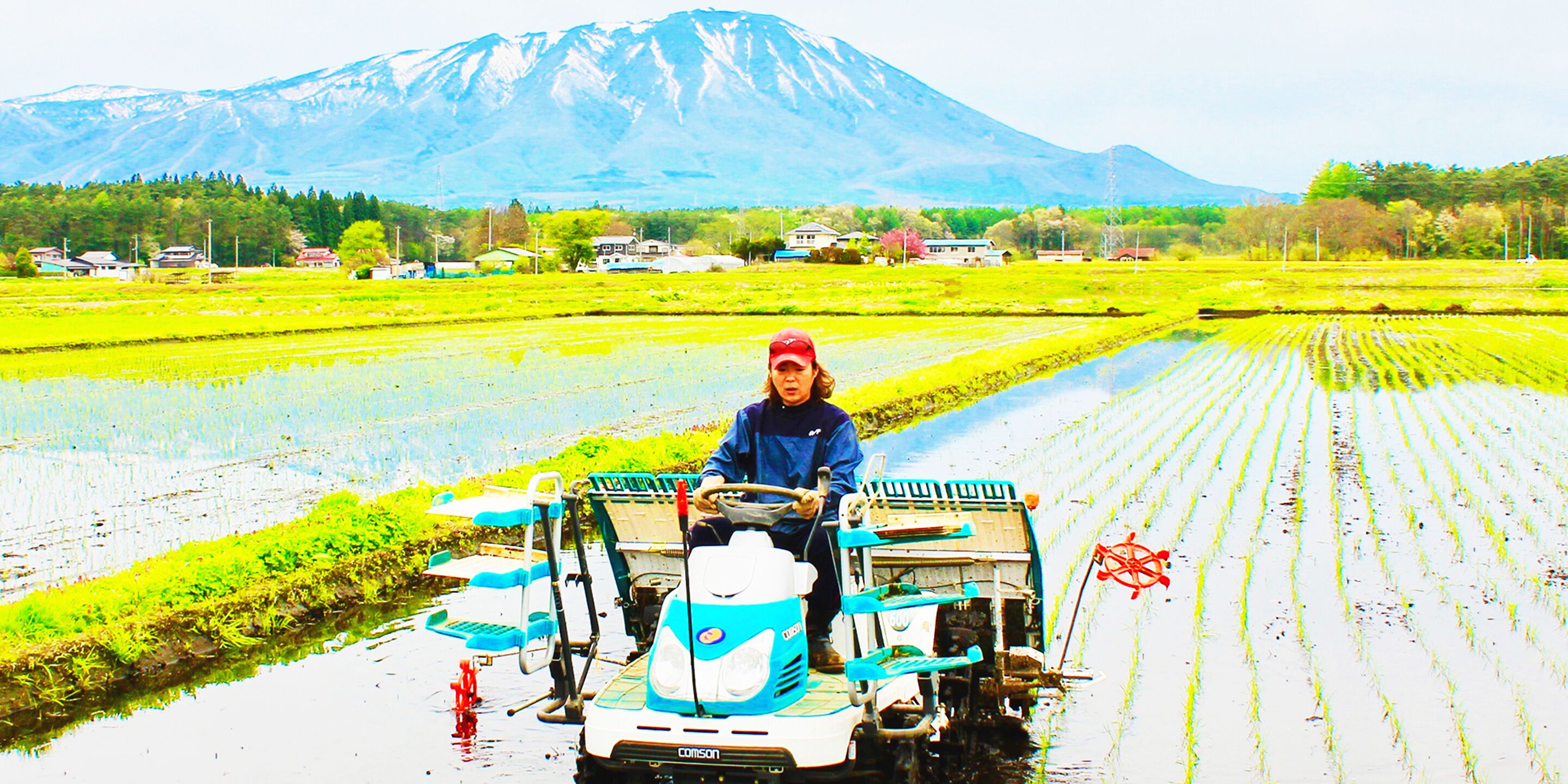 Una persona manejando una máquina agrícola impulsada por agua en un campo, con una montaña al fondo.
