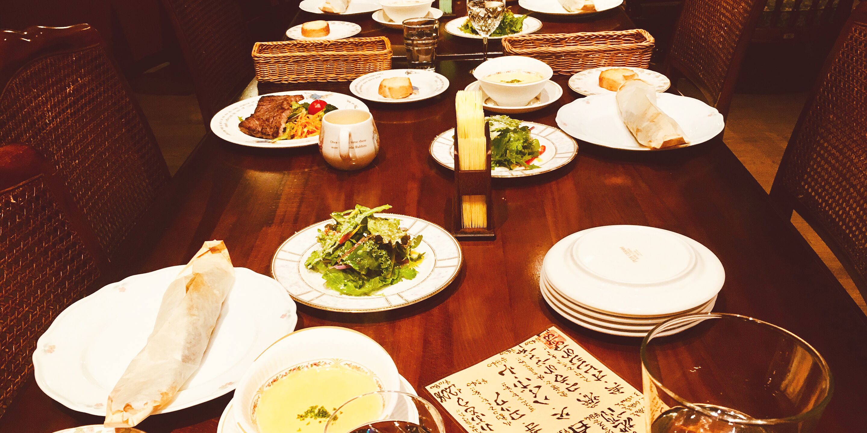 A dining table set with plates, bowls, and glasses, surrounded by wicker chairs.