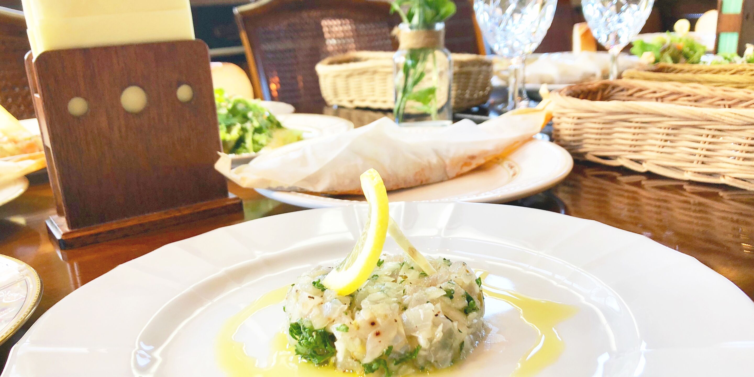 Una mesa de comedor con un plato blanco de comida, un vaso de agua y una cesta de mimbre.