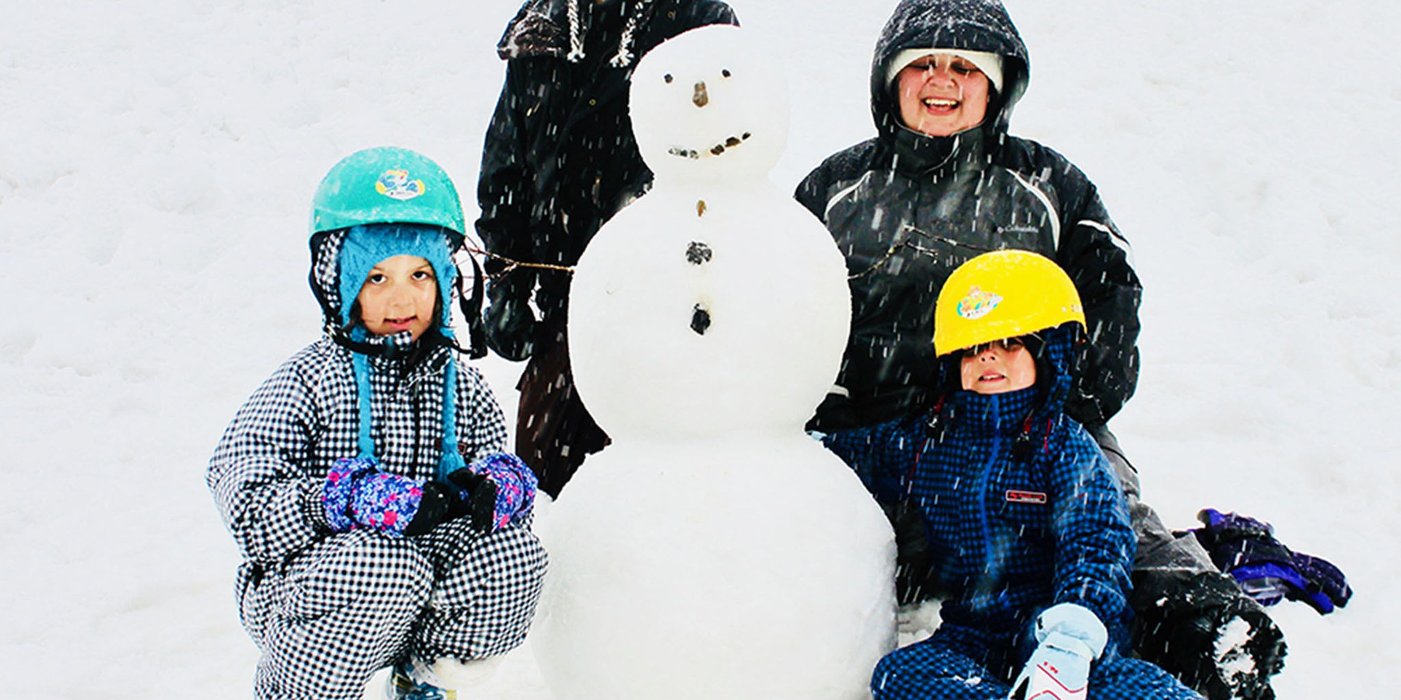 Tre barn sitter bredvid en snögubbe i en snötäckt utomhusmiljö.
